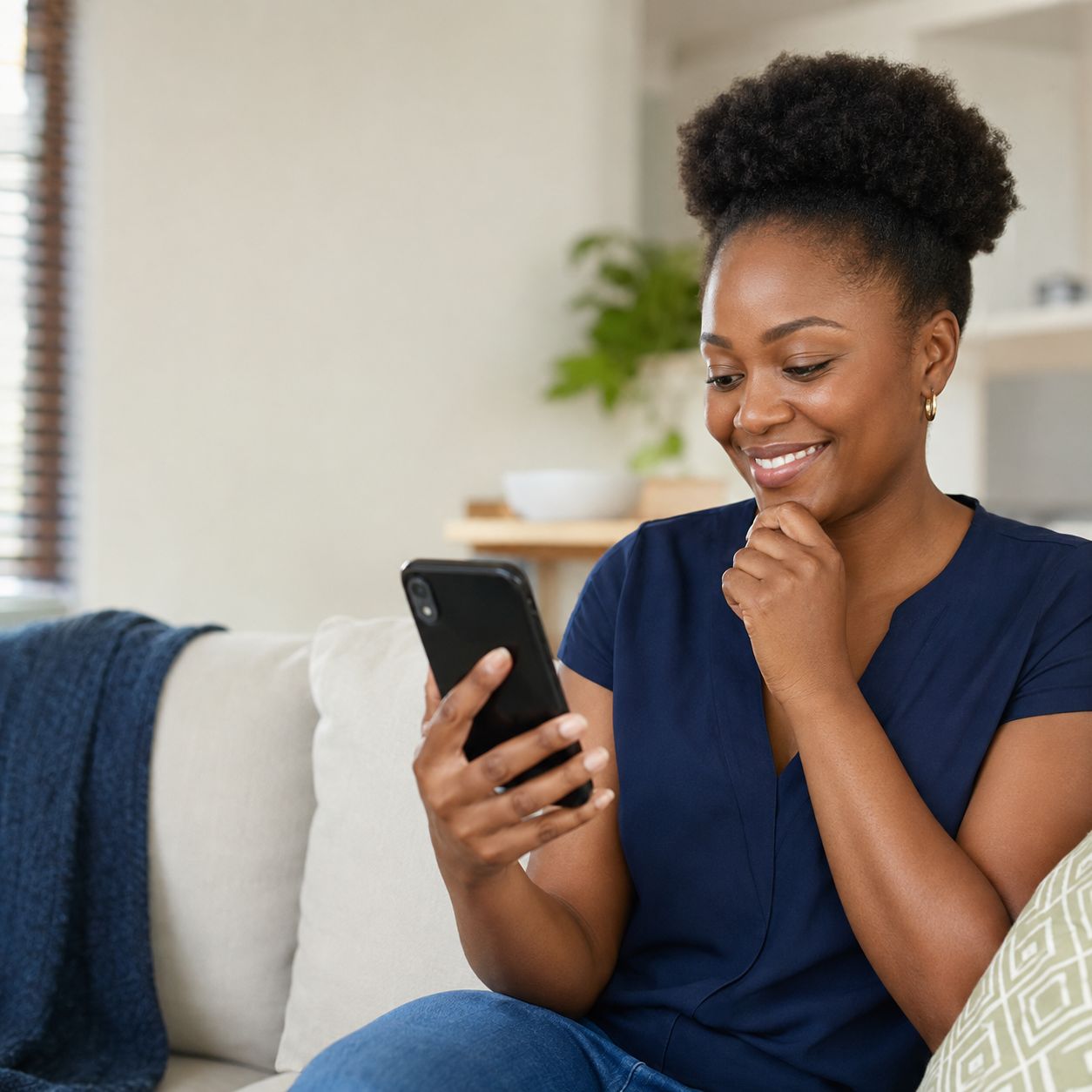 A woman smiles while reading an update on her phone from her couch.